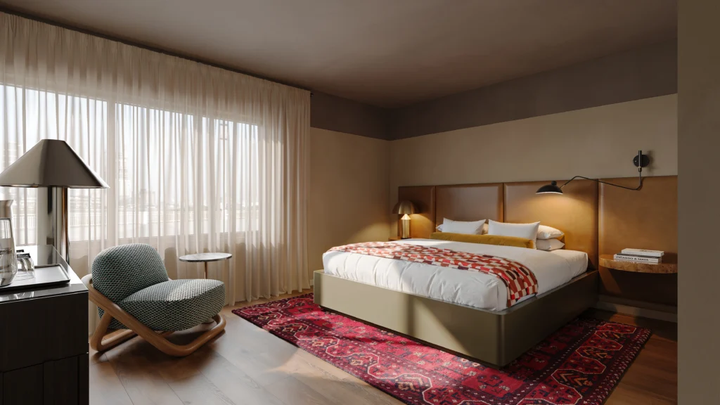 Bright hotel bedroom with king bed, patterned throw, red area rug, and sitting chair by a large window