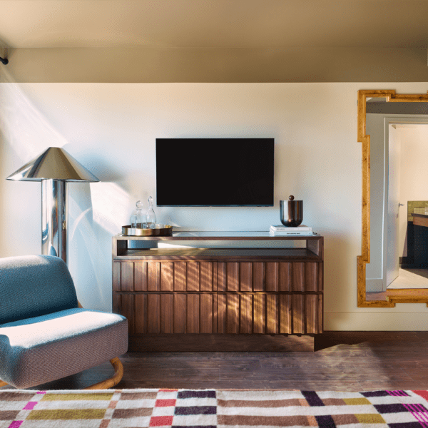 Modern hotel room with wall-mounted TV, wood cabinet, lounge chair, and sheer curtains in daylight